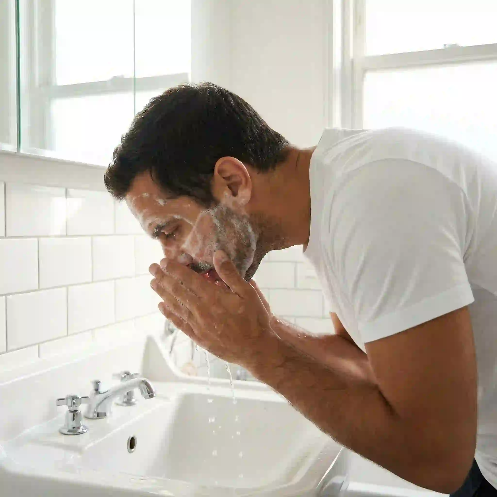 Man washing his face with gentle cleanser to remove oil, preparing the skin for beard removal cream application to ensure maximum contact with the hair and improve the effectiveness of the depilatory process.