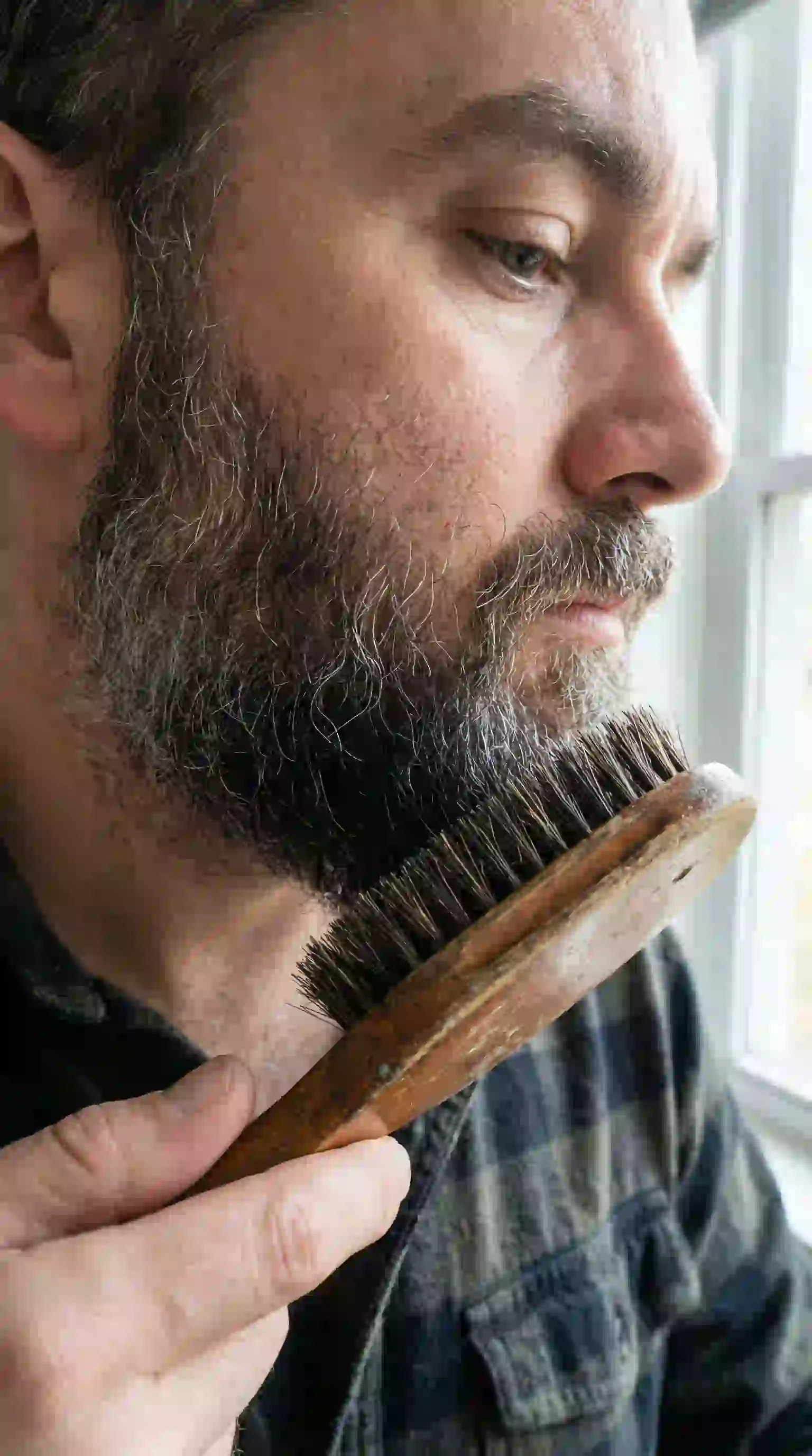 A man using a boar bristle brush to train his facial hair direction, a key technique for concealing gaps and learning how to remove patchy beard.